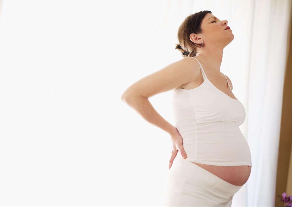 Kobieta w zaawansowanej ciąży trzyma się za plecy, ponieważ odczuwa ból