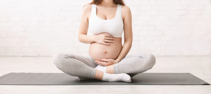 Kobieta w ciąży siedzi po turecku na macie i trzyma się za brzuch